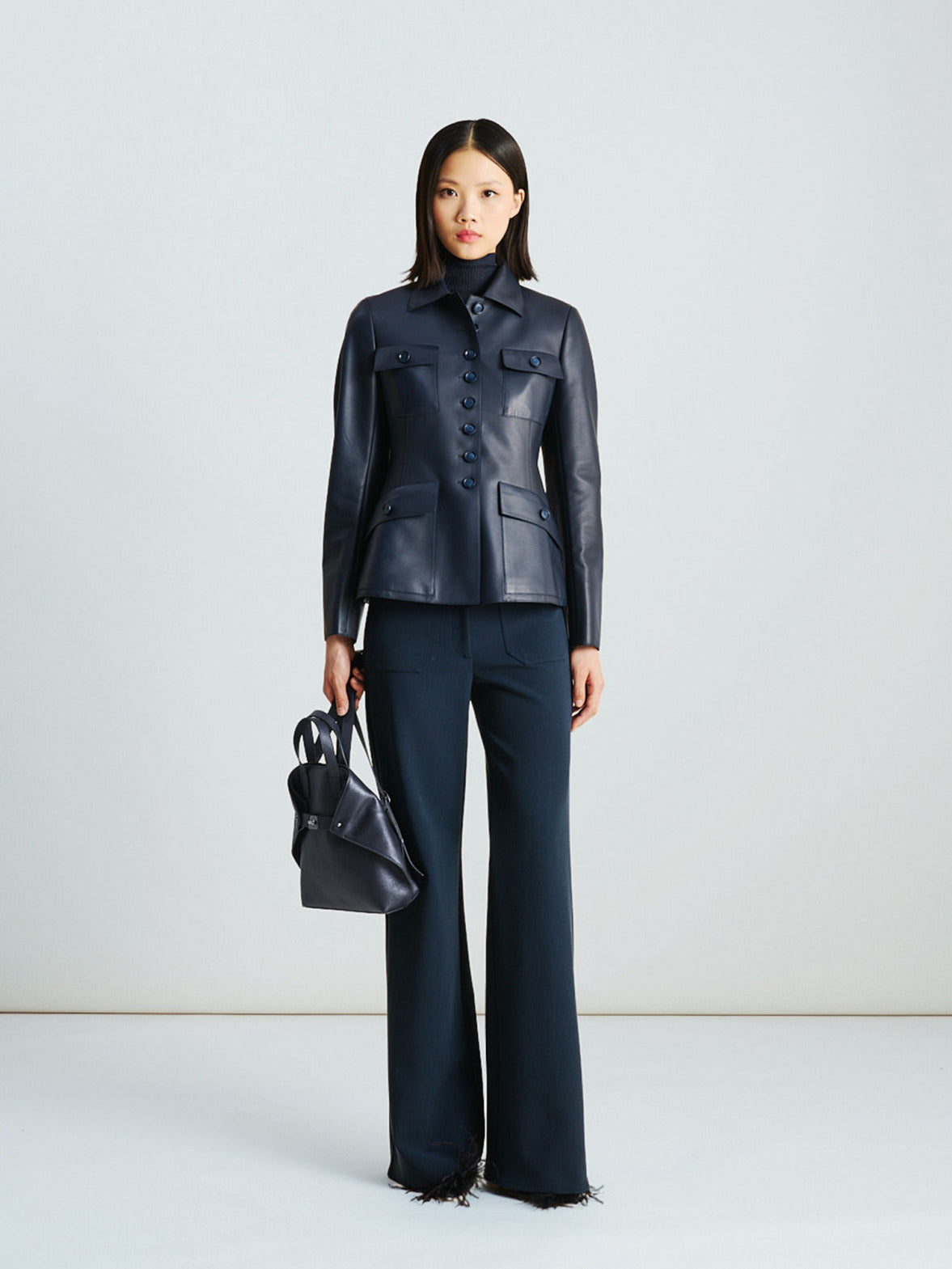 Akris Fall/Winter look in tonal denim blue — a fitted leather jacket with patch pockets paired with stretch wool bootcut pants, blending structure, softness, and understated luxury.