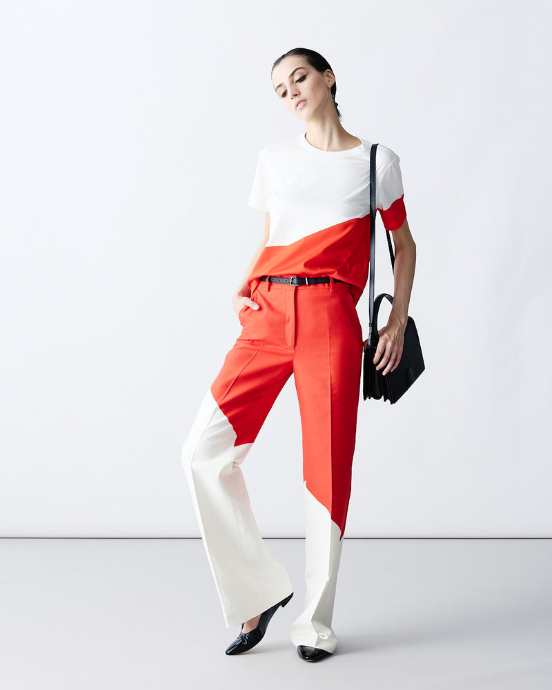 Detailed product shot of a matching red and white geometric color-block shirt and trousers set. The outfit is accessorized with a black belt and a structured black shoulder bag