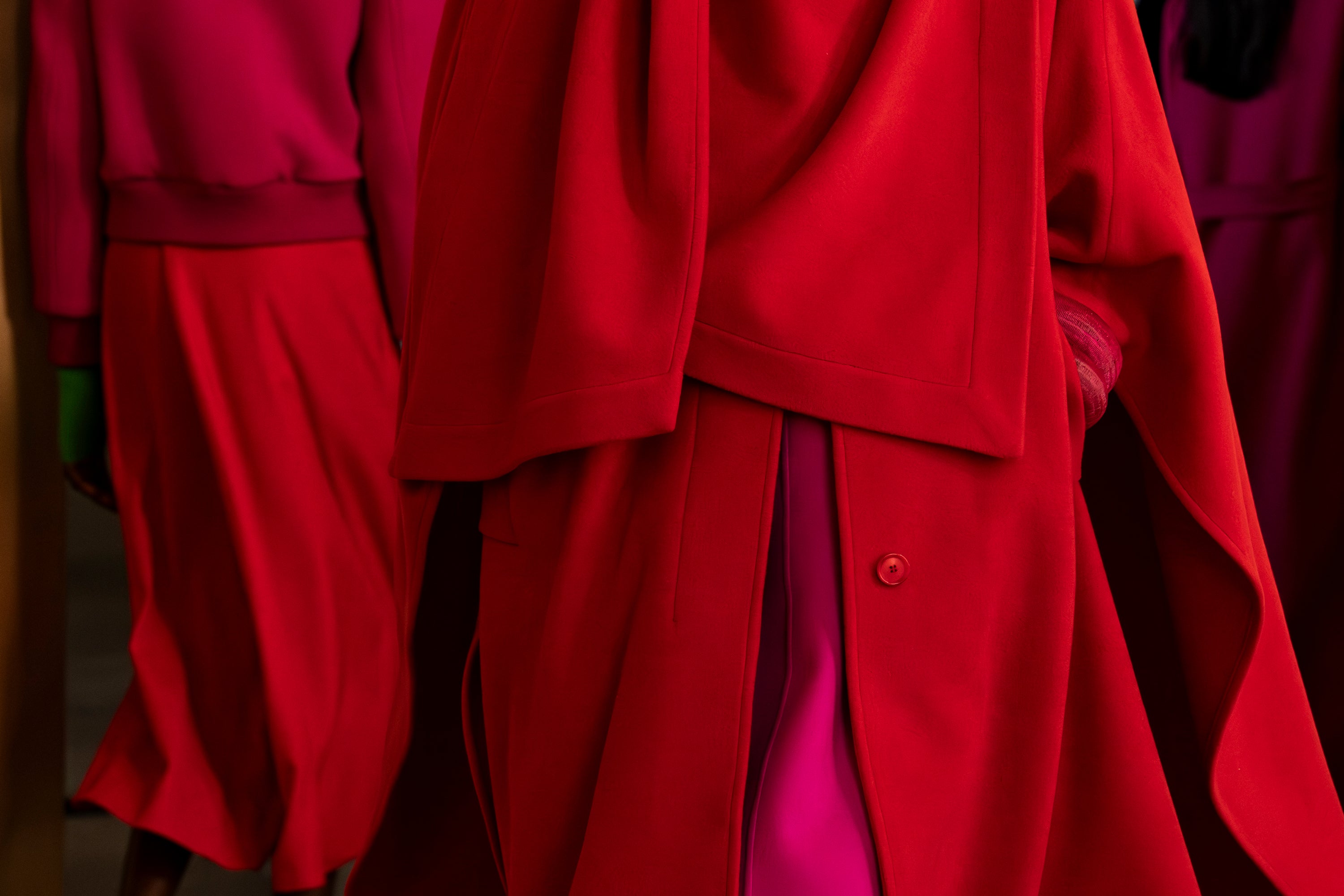 A vibrant close-up of layered wool garments in bold red and magenta hues, showcasing clean tailoring and rich monochromatic textures.
