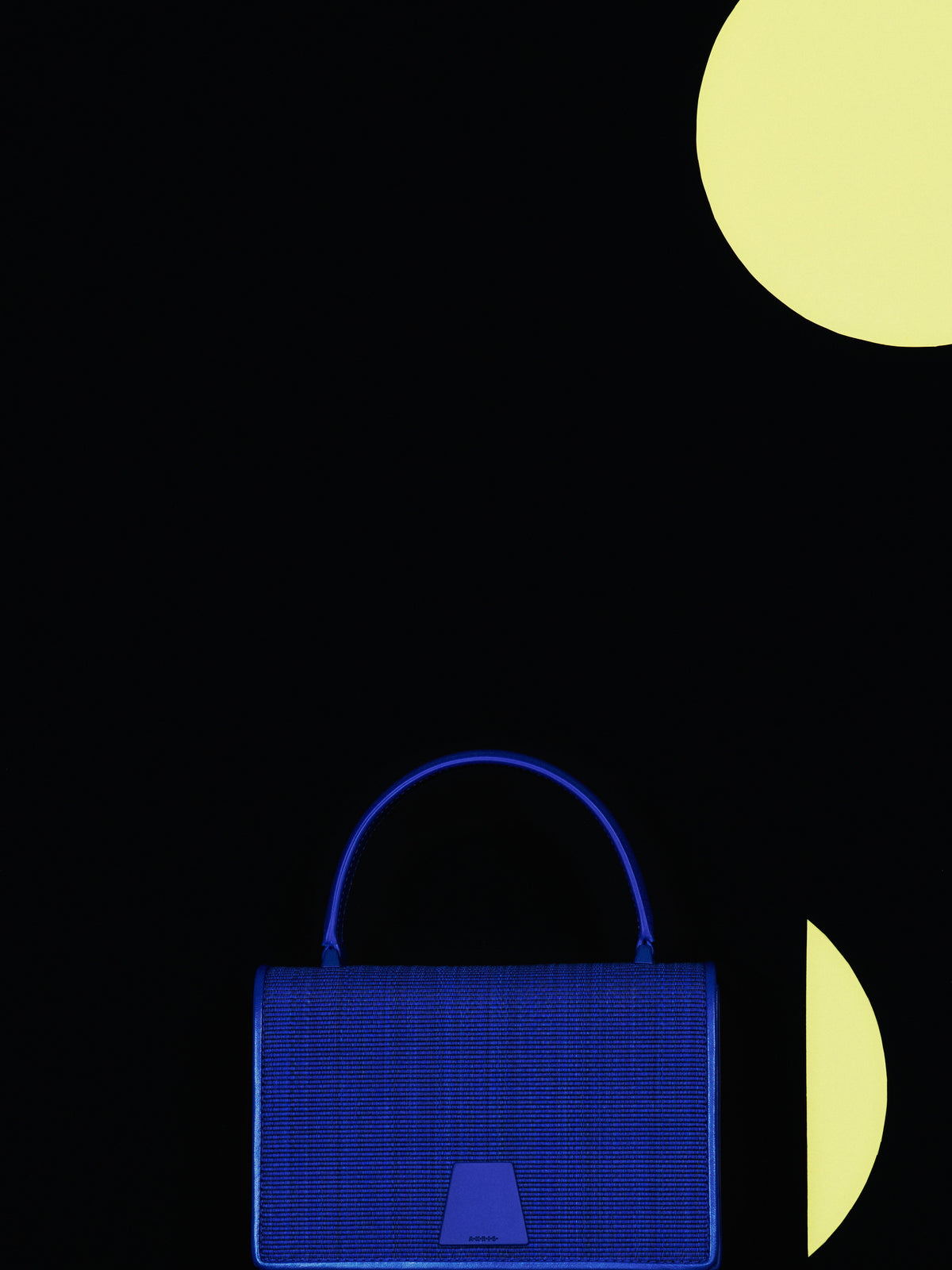 Discover the captivating texture of the Akris Pre-Fall collection, showcasing the elegant Alice handbag crafted in a brilliant electric blue horsehair. Strikingly set against a deep black backdrop accented with soft yellow geometric shapes, this luxury piece combines sculptural form with unique artisanal material. Experience modern sophistication and premium Swiss design.