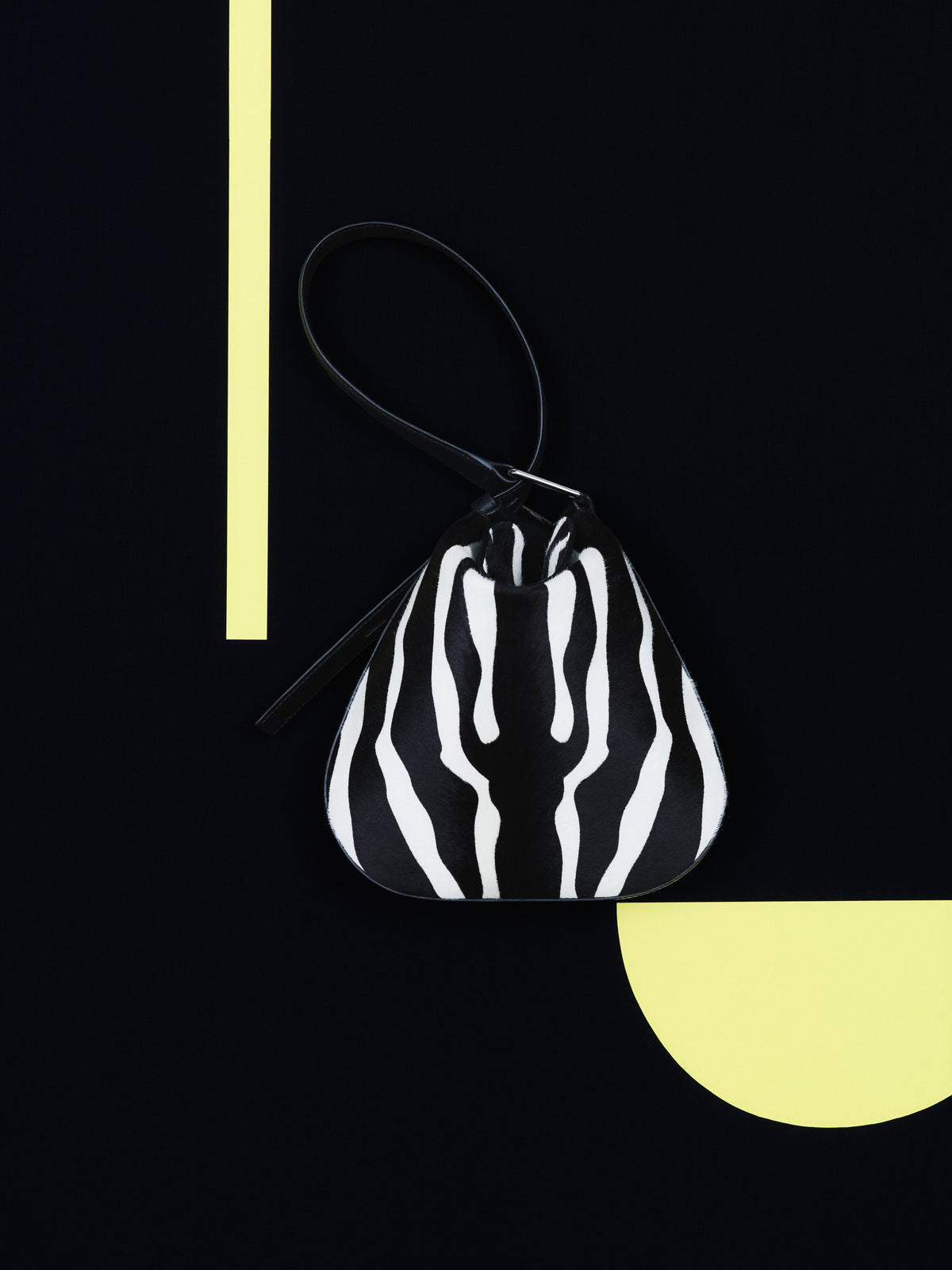 Discover the bold elegance of the Akris Pre-Fall collection, showcasing the sophisticated Anna Hobo bag in a striking zebra print. Artfully presented against a minimalist black backdrop with pale yellow geometric accents, this luxury piece features a unique slouchy silhouette. Experience modern refinement and premium Swiss craftsmanship.
