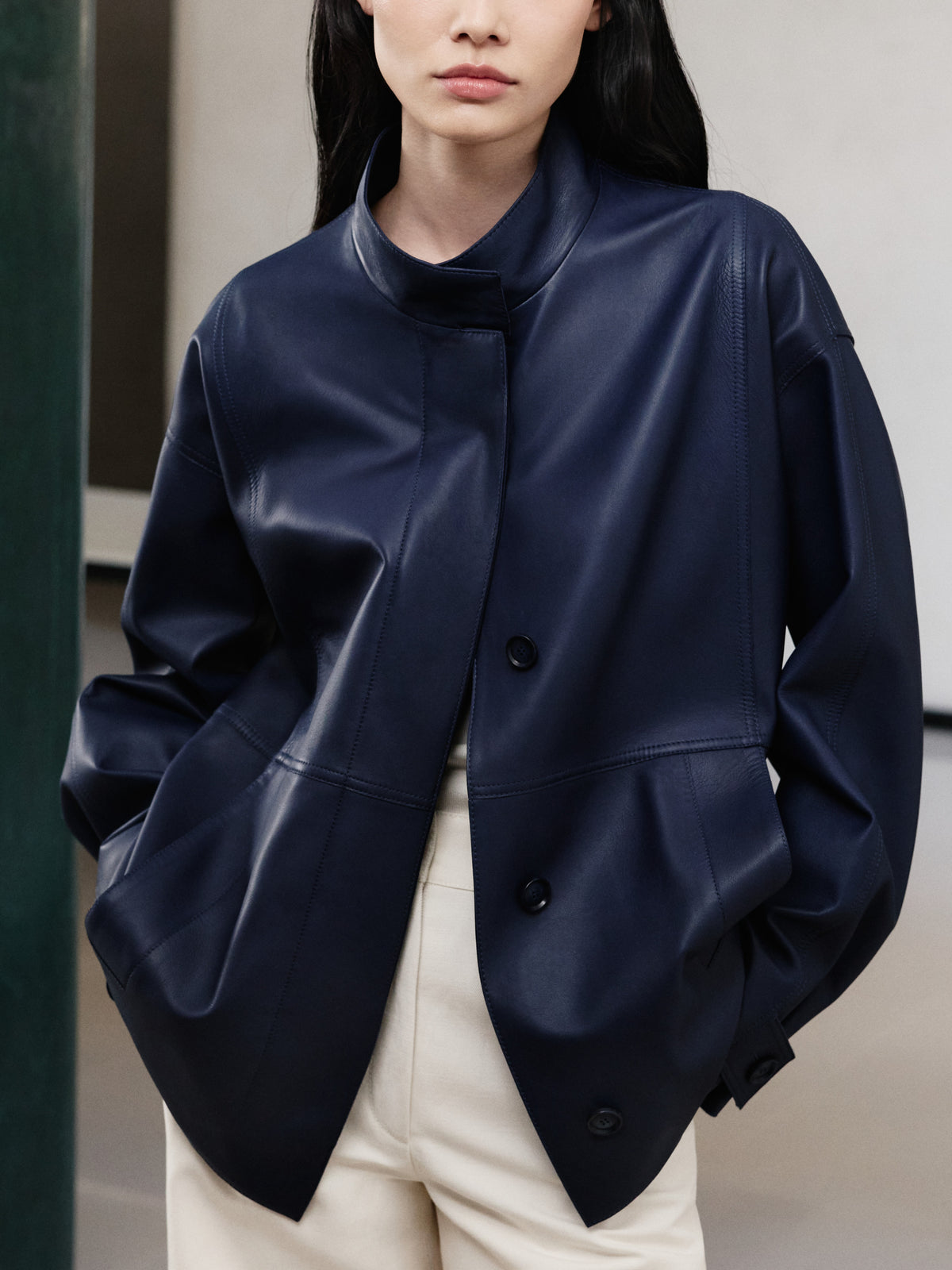 Discover the modern tailoring of the Akris Pre-Fall collection, showcasing an oversized luxury leather jacket in a deep navy blue hue. Detailed with a sleek stand-up collar and structural seams, it pairs perfectly with cream-colored trousers. Elevate your look with understated elegance and premium Swiss craftsmanship.