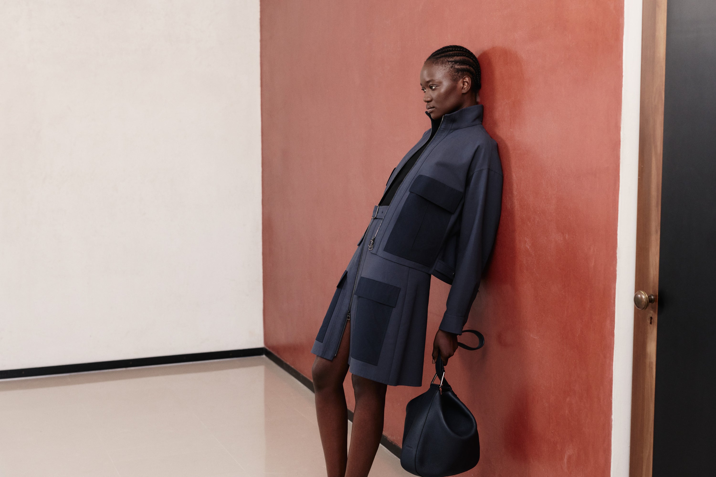 Discover the modern utilitarian aesthetic of the Akris Pre-Fall collection, showcasing a structural jacket and skirt set in deep navy blue with tone-on-tone pockets. This monochromatic ensemble is casually paired with a slouchy luxury handbag for a contemporary finish. Explore innovative, fluid tailoring and premium Swiss craftsmanship.