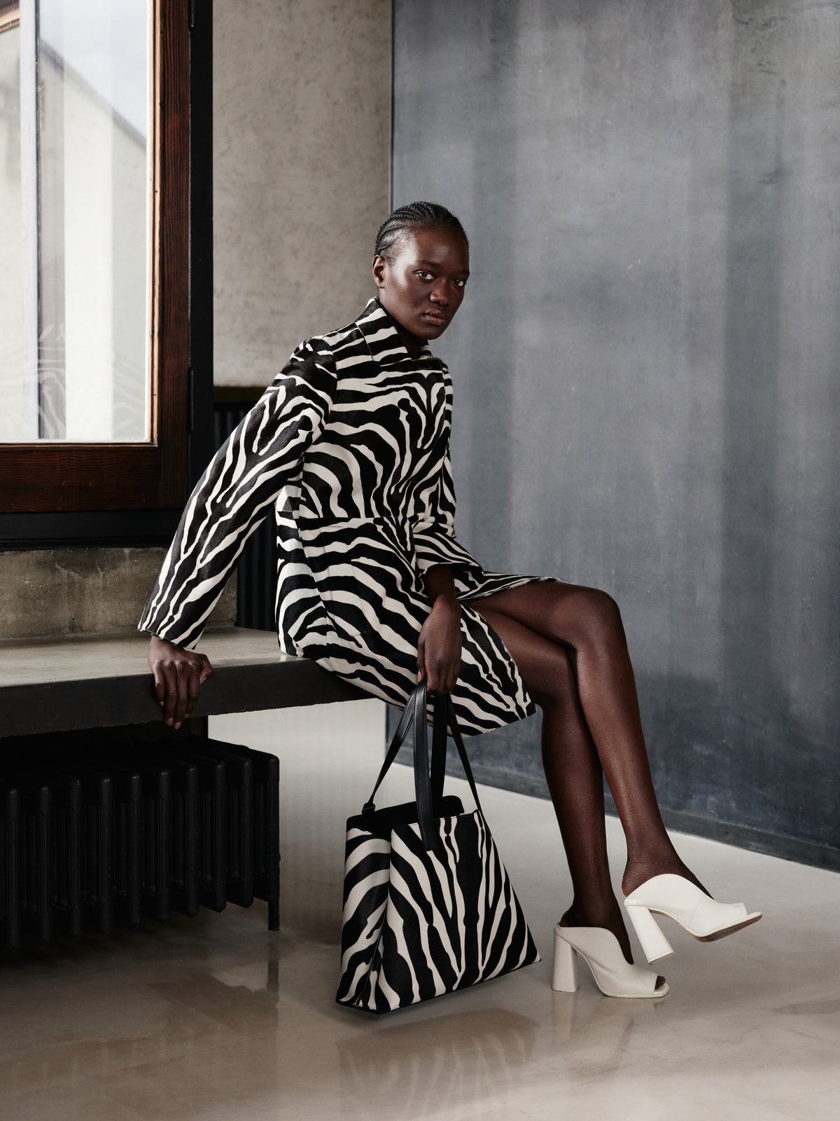 Embrace high-contrast sophistication with the Akris Pre-Fall collection, highlighting a statement coat in a bold zebra print. Complete the striking look with the matching Ai tote bag and elegant white leather mules for a touch of modern contrast. Discover luxury tailoring that seamlessly merges bold graphics with Swiss artistry.