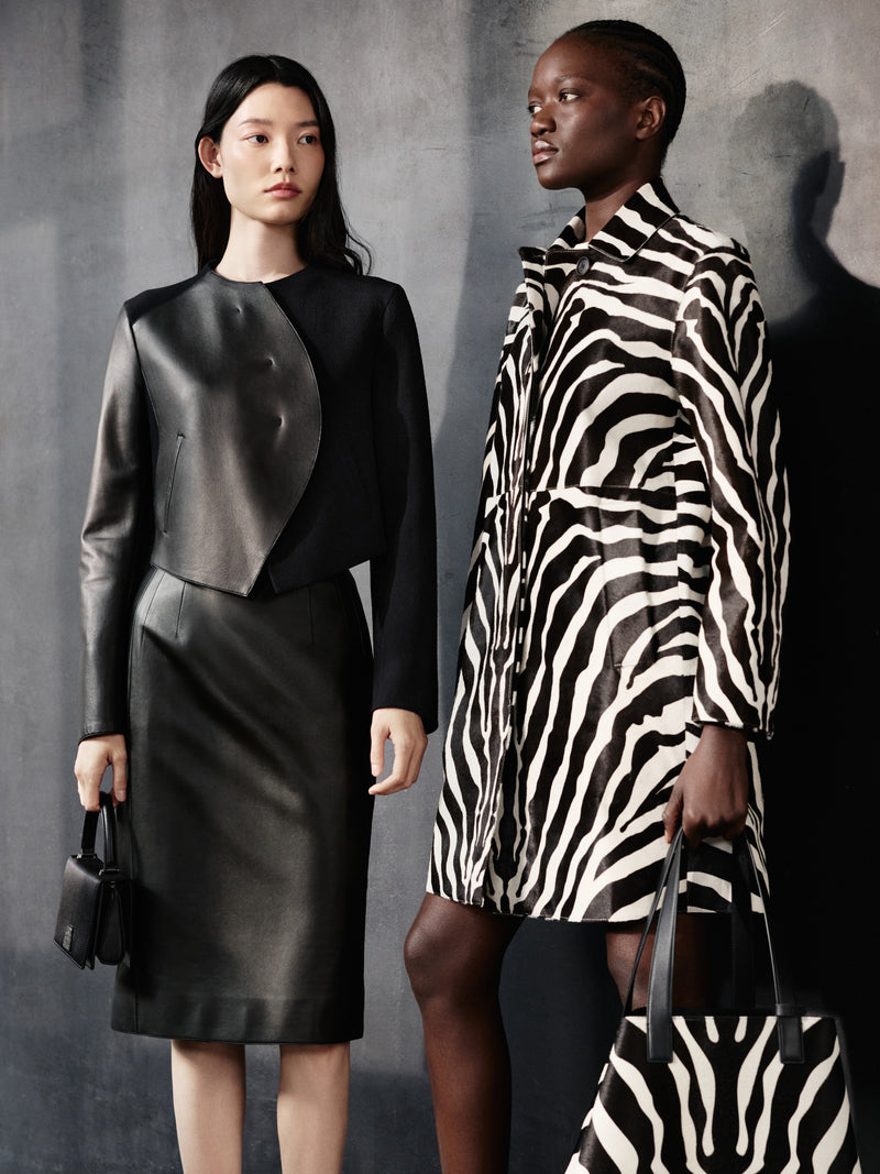 Explore the striking contrasts of the Akris Pre-Fall collection, featuring a structural black leather jacket and skirt set alongside a bold, full-length zebra print coat. Complete your style with the coordinating luxury handbags, including the iconic Ai tote and the elegant Anouk. Discover exquisite Swiss tailoring designed for modern elegance.