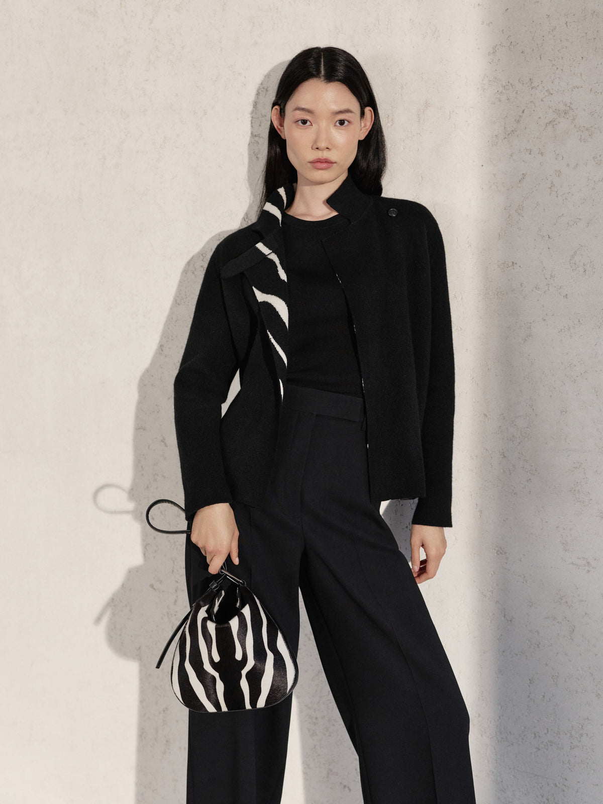 Discover the sophisticated versatility of the Akris Pre-Fall collection, featuring a tailored black ensemble with a subtle zebra-accented collar. Complete the look with the graphic elegance of the Anna Hobo handbag in a matching zebra print. Experience the perfect harmony of modern design and Swiss craftsmanship.