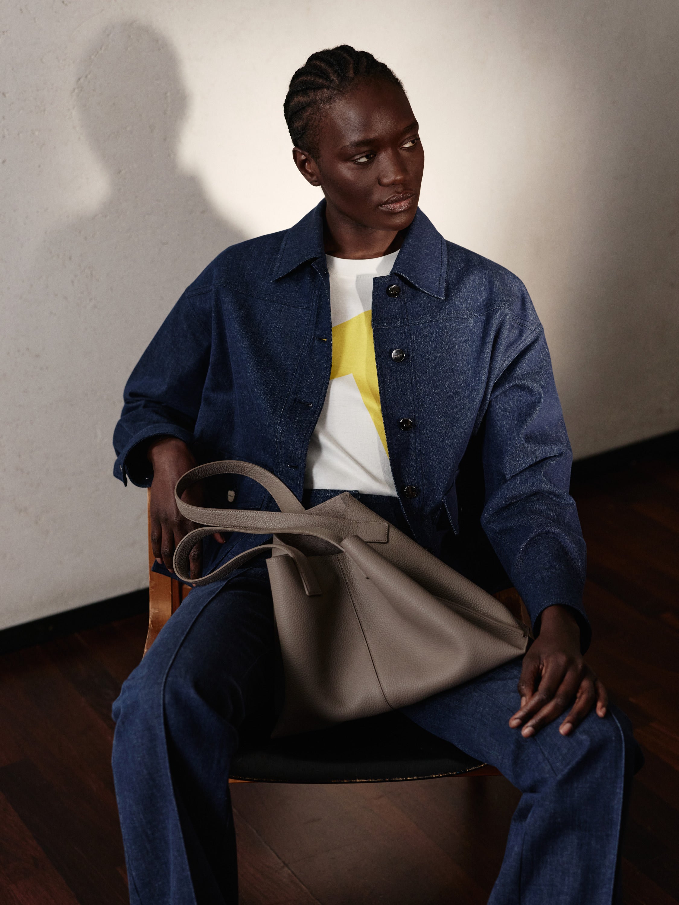 Discover the casual luxury of the Akris Pre-Fall collection, highlighting a premium denim jacket paired with a vibrant yellow-accented top. The contemporary ensemble is completed by the iconic Ai tote bag in a versatile taupe leather finish. Elevate your daily style with modern essentials and timeless Swiss craftsmanship.