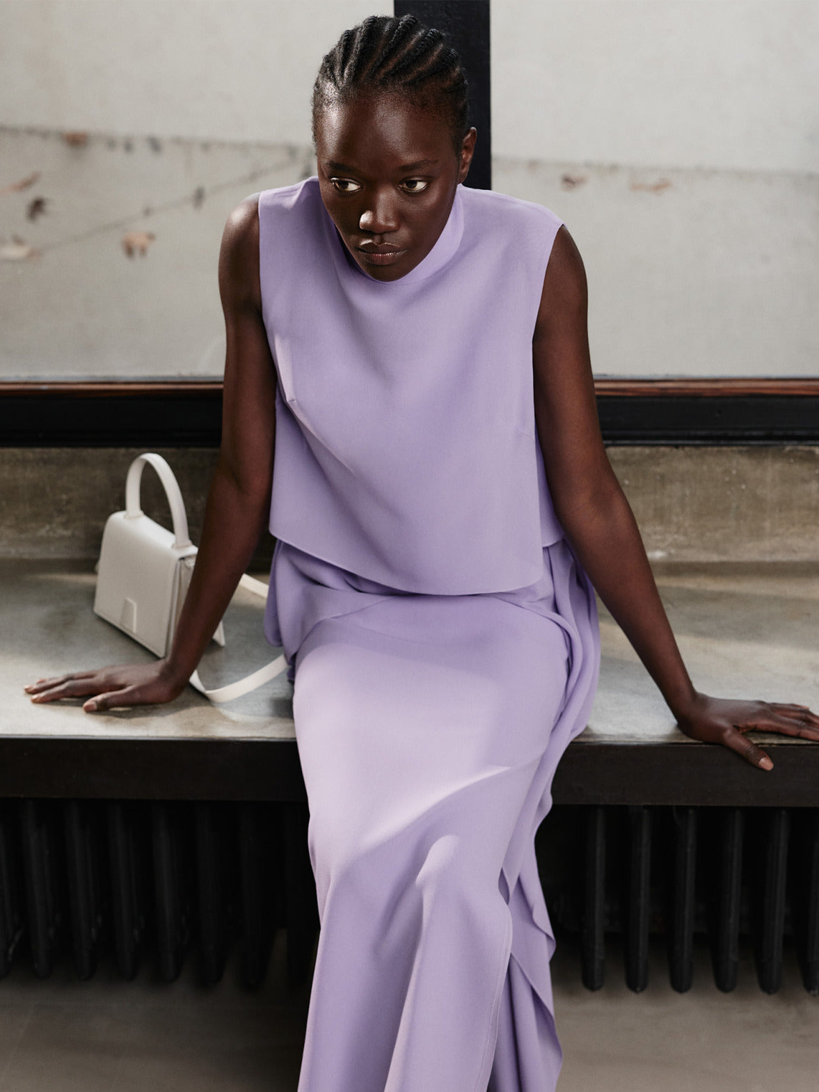 Model wearing a Malva dress and top from the Akris Pre-Fall 2026 collection, paired with a white handbag and white heeled sandals.