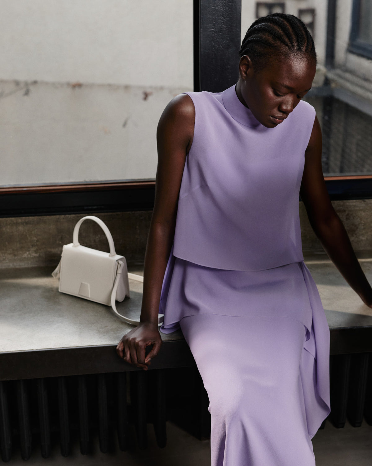 Akris Pre-Fall 2026 luxury fashion collection showcasing a lavender sleeveless top with a high neckline.
The matching draped lavender skirt creates an elegant monochrome ensemble.
Accompanied by a structured off-white leather handbag with a top handle and shoulder strap.
