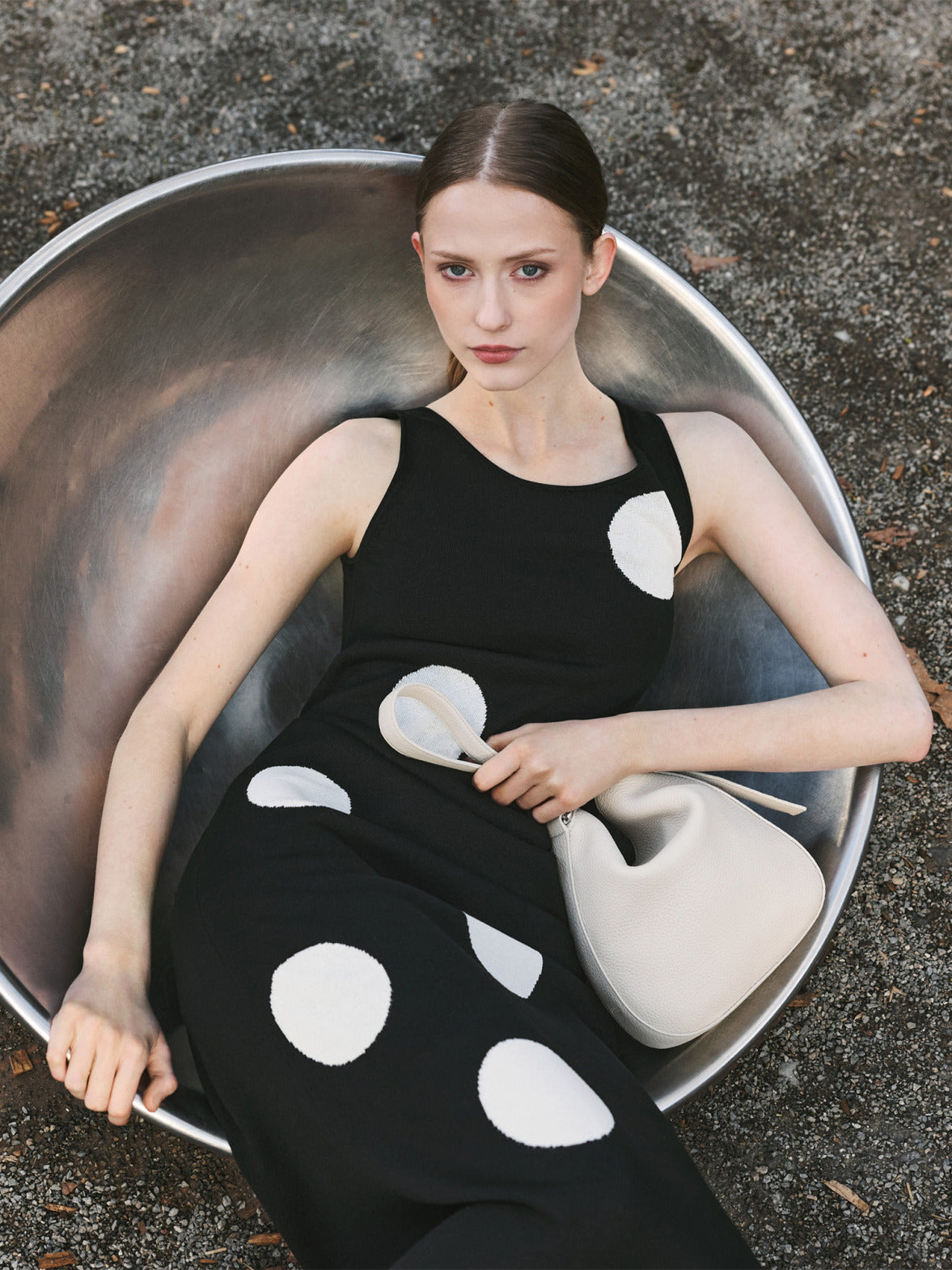 Model in a black Akris Pre-Fall 2026 knitted sleeveless polka-dot dress, holding an ivory leather bag.