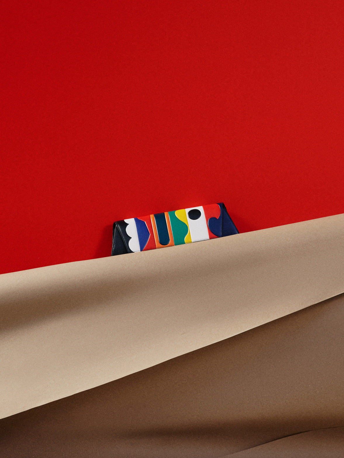 AI-generated 'Anouk' geometric panel evening bag peeking from brown paper on a red background.