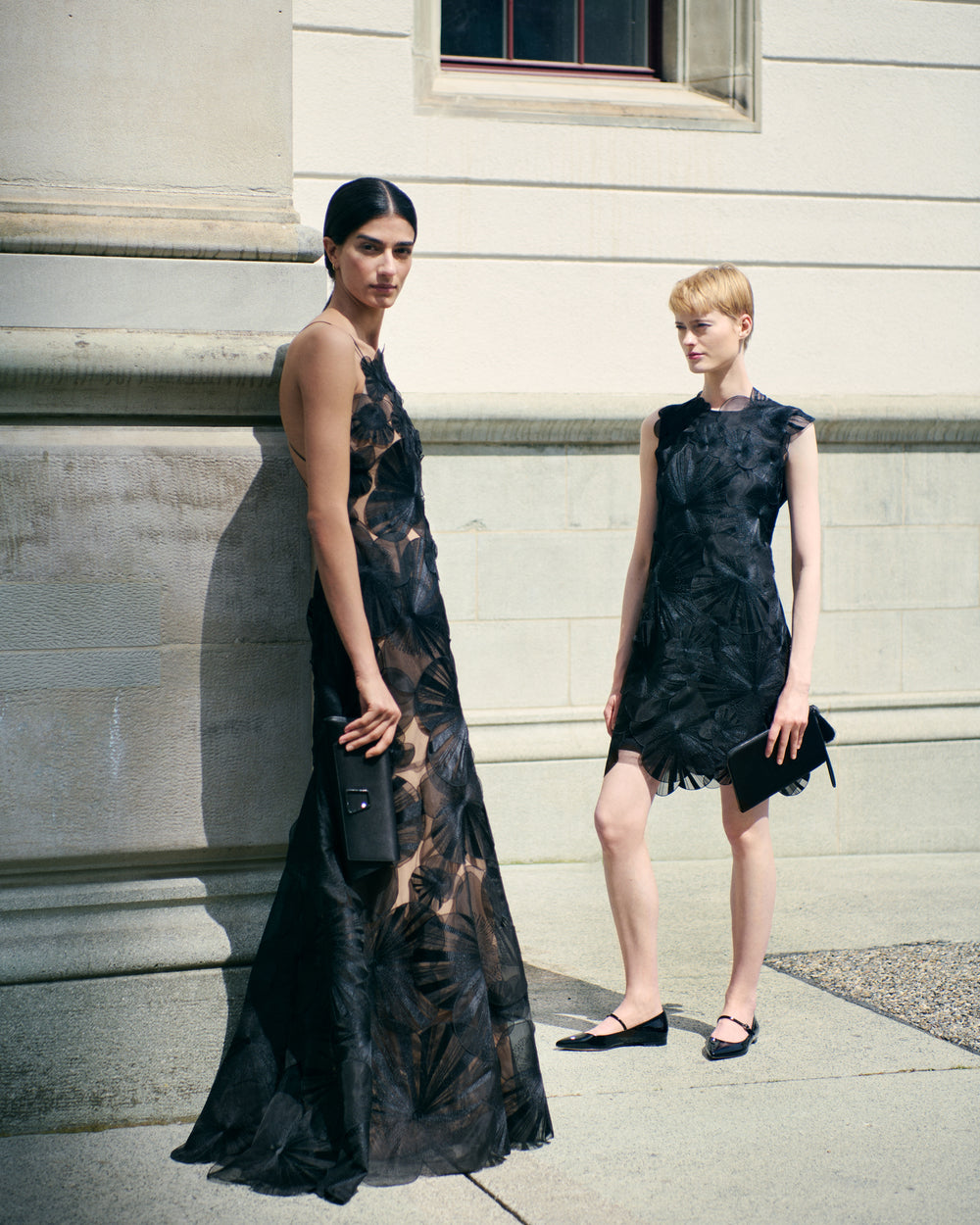 Two Women, dressed in elegant black embroidery evening gowns of Akris, stand in front of an old building.