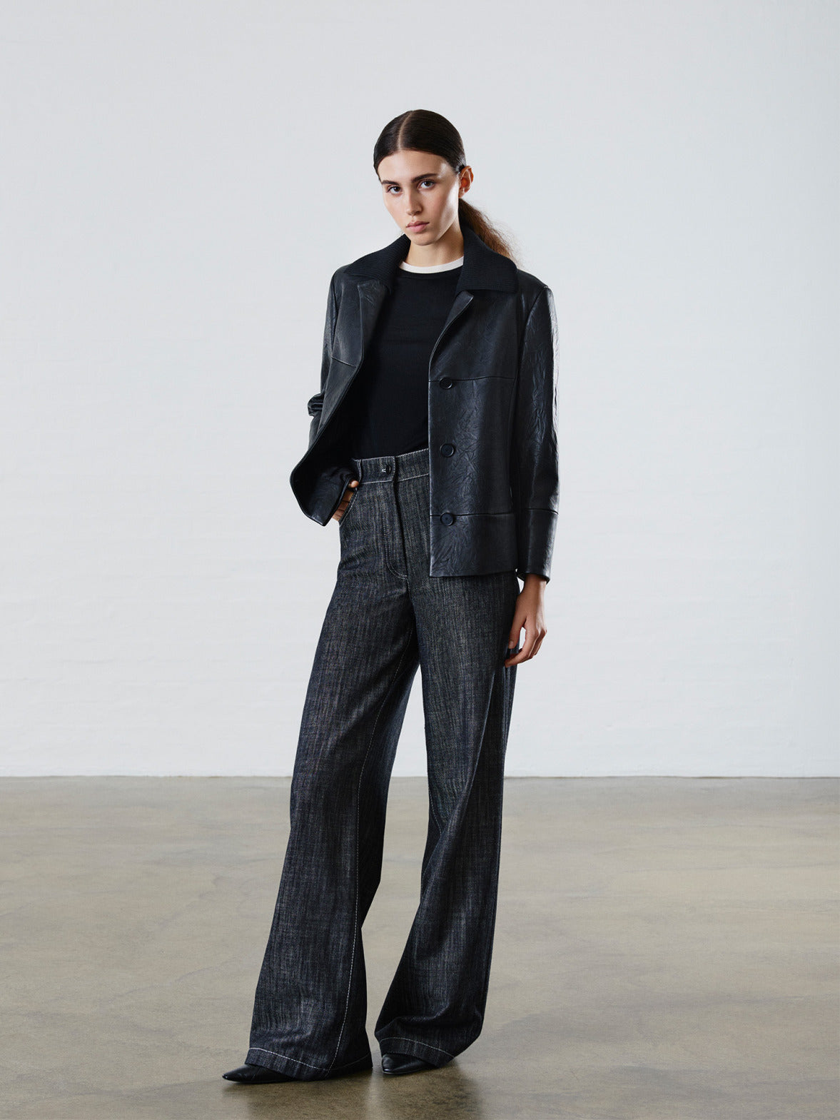 Luxury "Denim Vibes" campaign: Model posing in a premium black leather jacket with a knit collar, paired with high-waisted dark grey denim trousers.